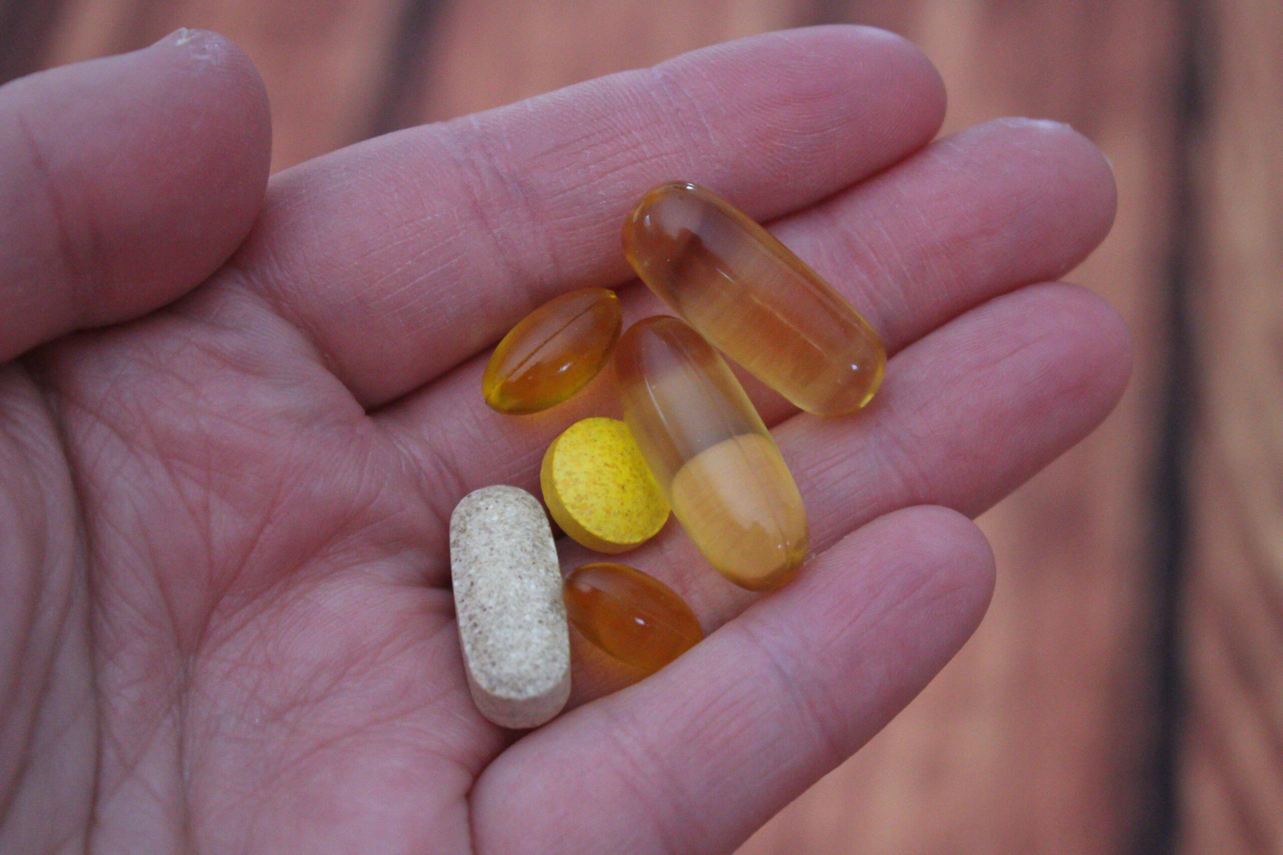Hand holding a selection of multivitamin tablets and capsules for men over 40