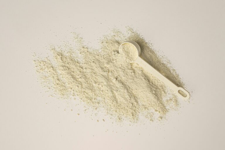 Whey protein powder spilled with a measuring scoop on a white background