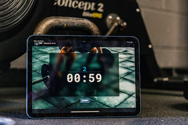 Tablet showing a workout timer app in a home gym next to a kettlebell and rowing machine