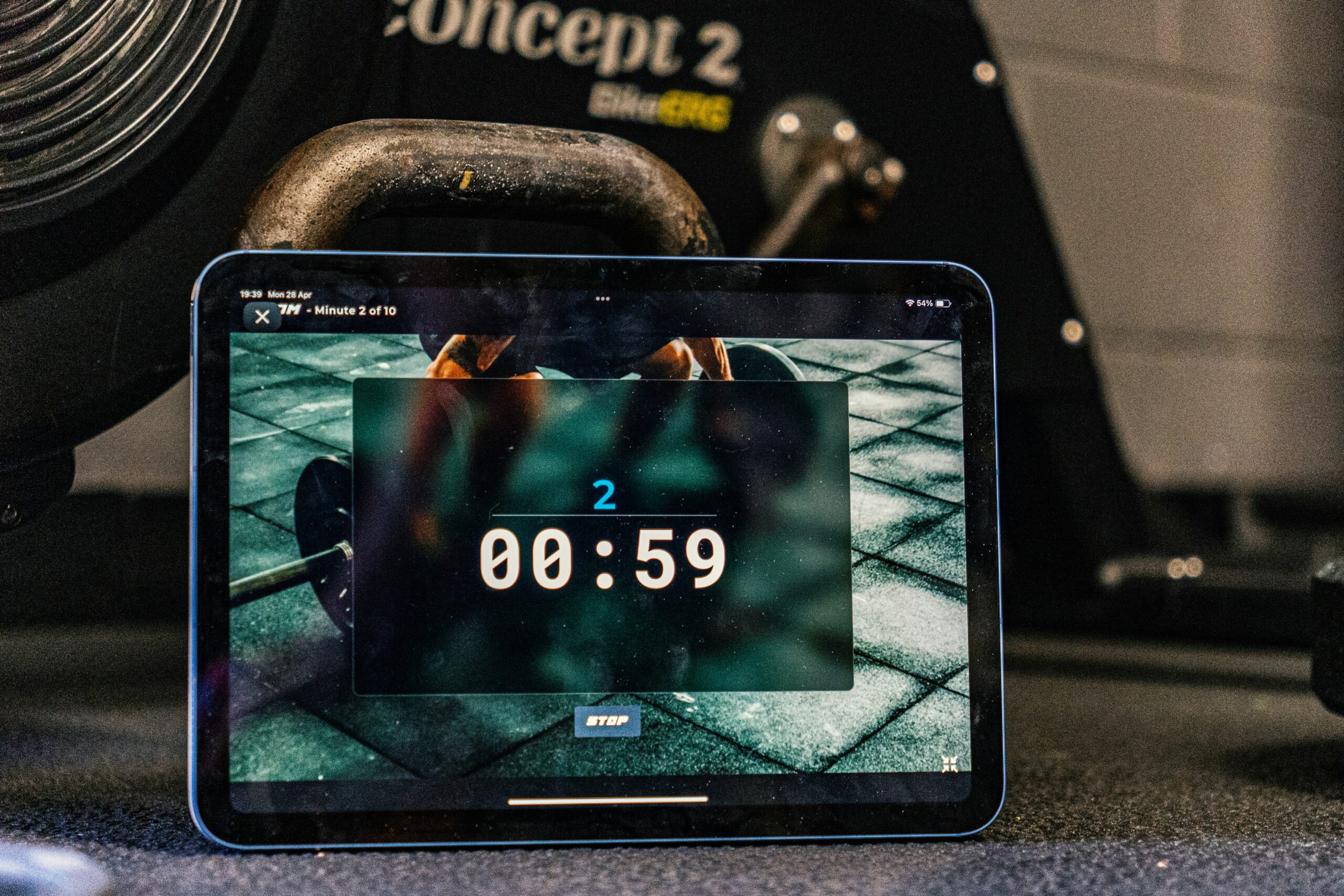 Tablet showing a workout timer app in a home gym next to a kettlebell and rowing machine